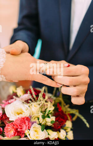 Close-up view of the groom`s hands putting the ring on the finger of the bride. Stock Photo